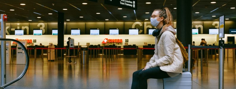 woman sitting on luggage at airport with mask