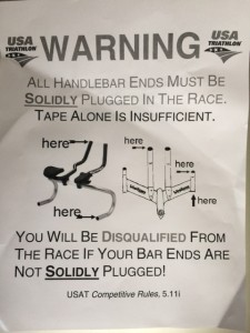 This sign reminds riders to ensure their bike handles are properly plugged before a race.