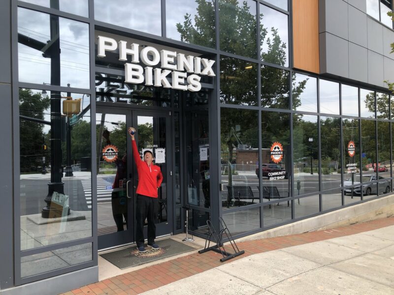 Mr. Landau posing in front of Phoenix Bikes shop. Image shows pretty all glass exterior of the business.