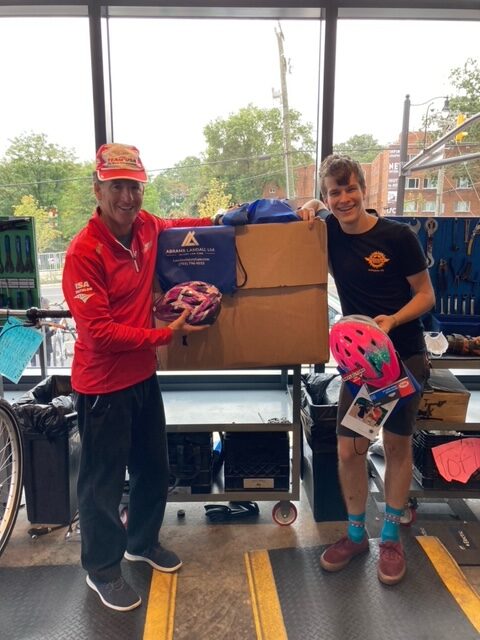 Attorney Doug Landau and Program Coordinator Liam, posing in the bike shop with some of the helmets donated by Abrams Landau, Ltd.